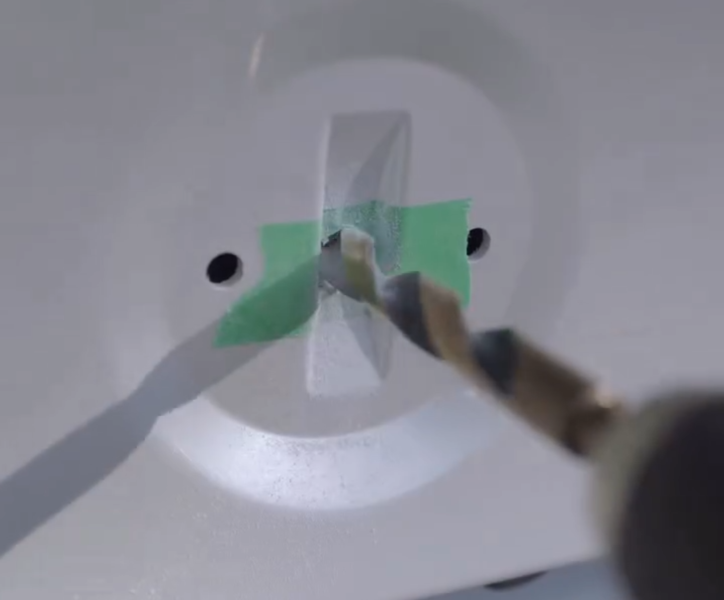 A drill bit going through masking tape into a car boot lid to fit an alternative badge