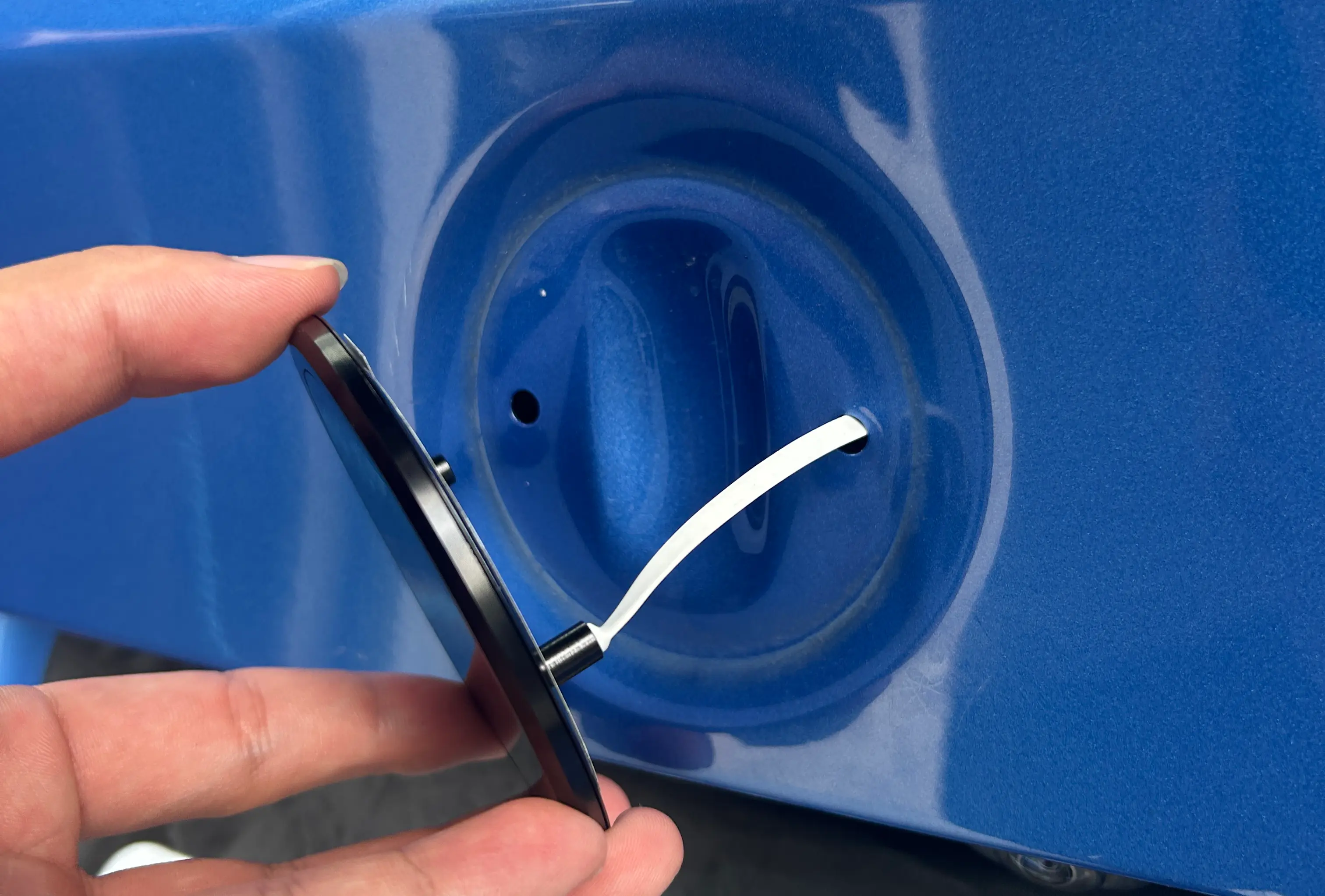 A hand pressing the emblem into the factory recess, its lead passing through an existing hole
